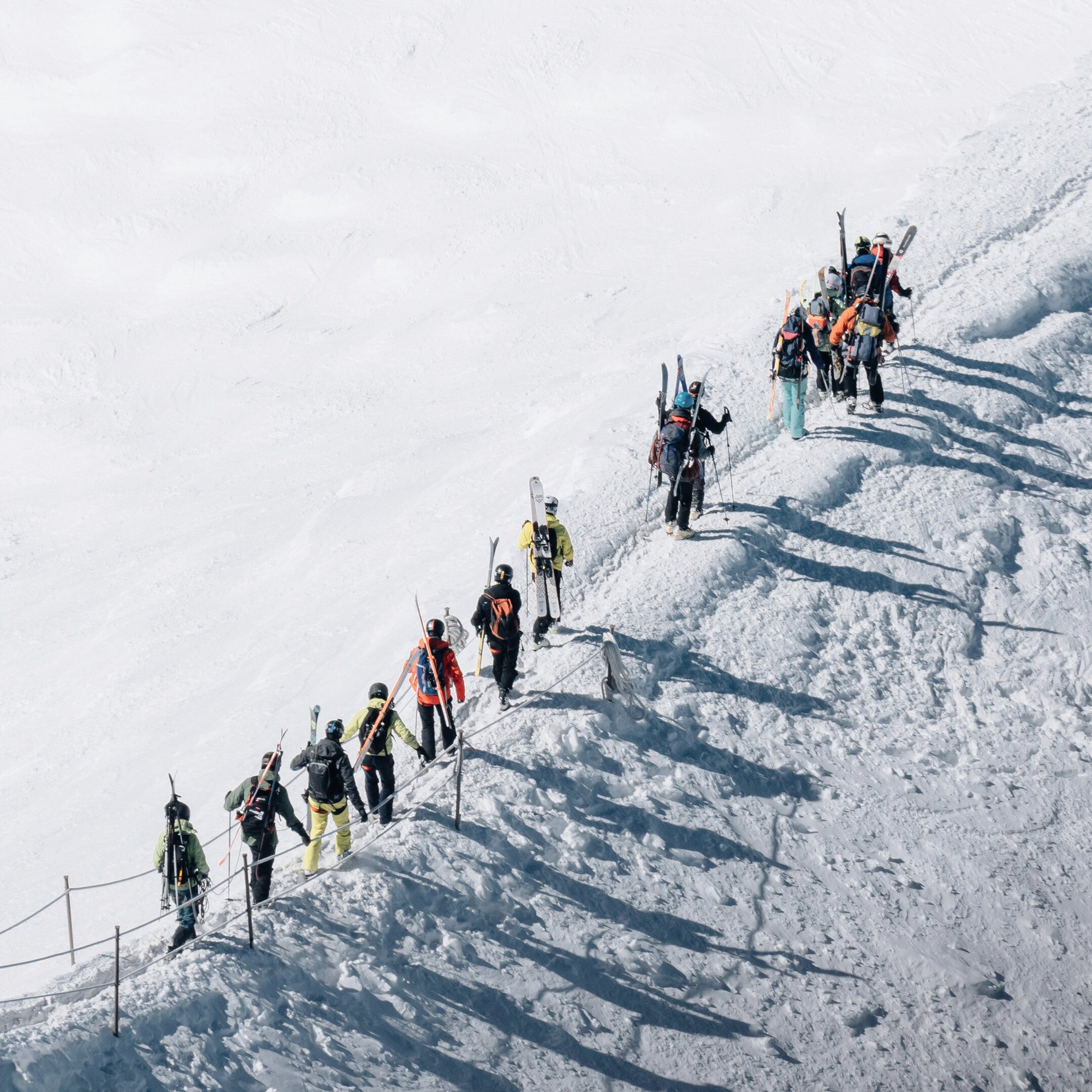 picture taking using drone up in the sky in mountains full of snow with people walking in a snowy trail.