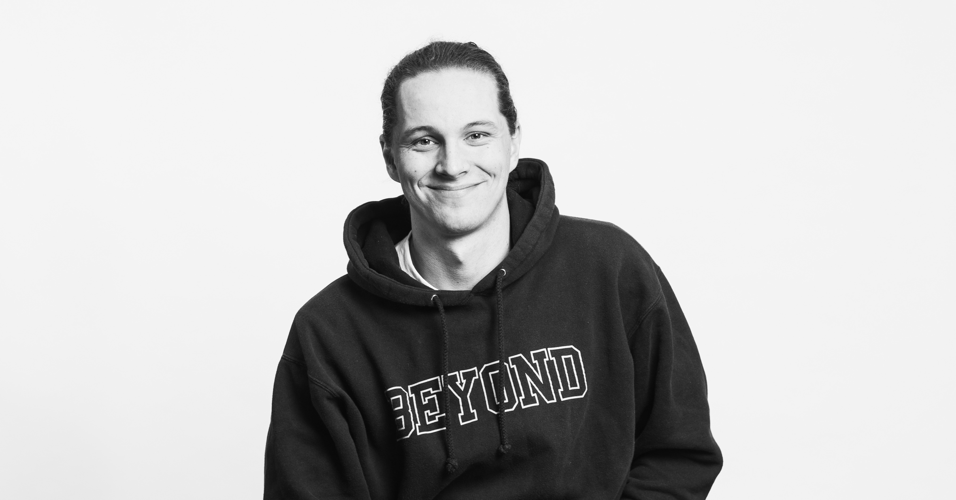A black and white photo of a smiling person with a black hoodie. 