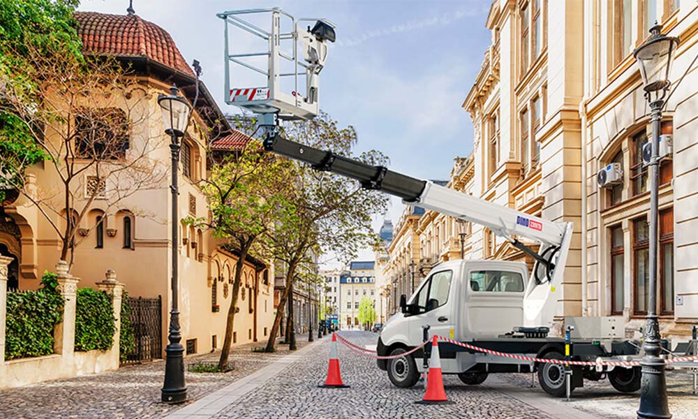 A vehicle mounted aerial work platform stood in the middle of a cobblestone street, surrounded by historic buildings.