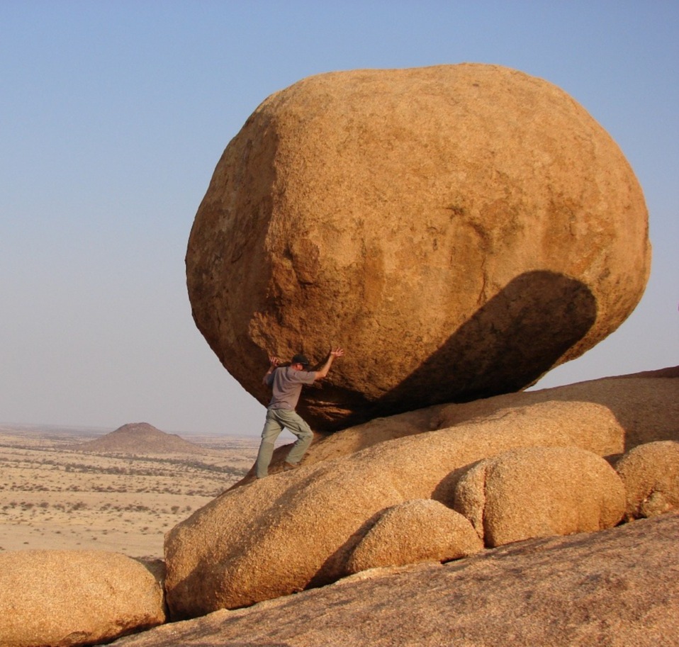 Mies kannattelee suurta kivenlohkaretta aavikolla